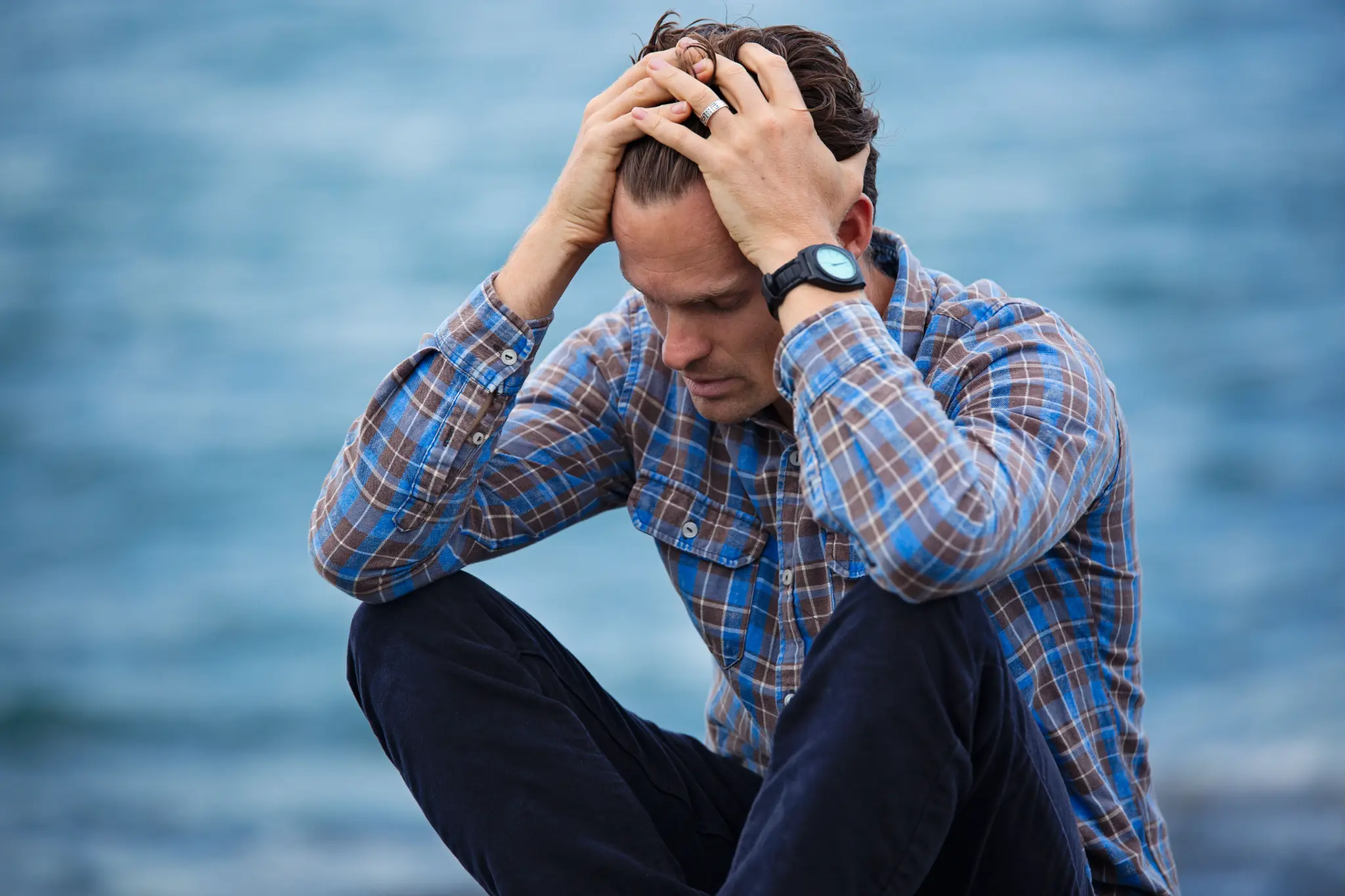 Man sitting by water with head in hands — grief counseling Los Angeles